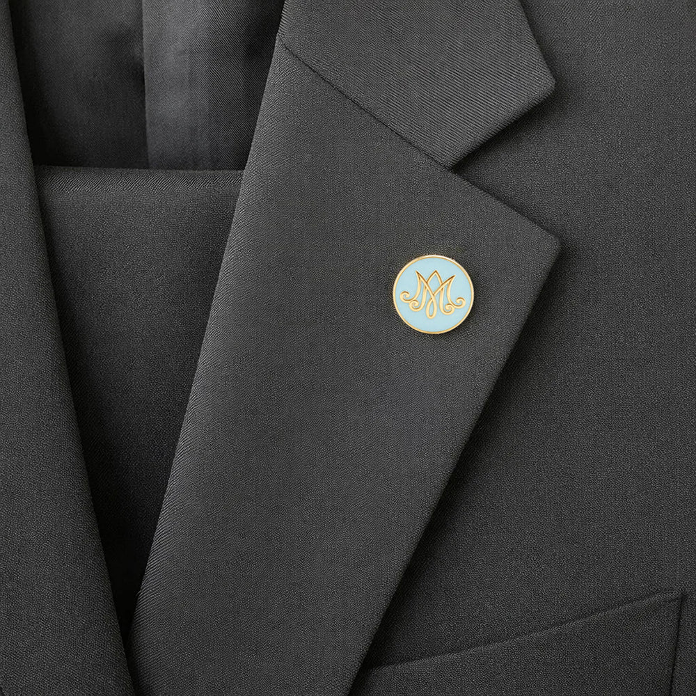 Close-up of a black blazer with a round, light blue pin featuring a logo on the lapel.