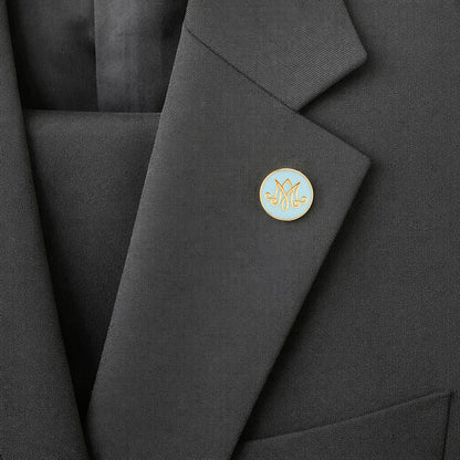 Close-up of a black blazer with a round, light blue pin featuring a logo on the lapel.