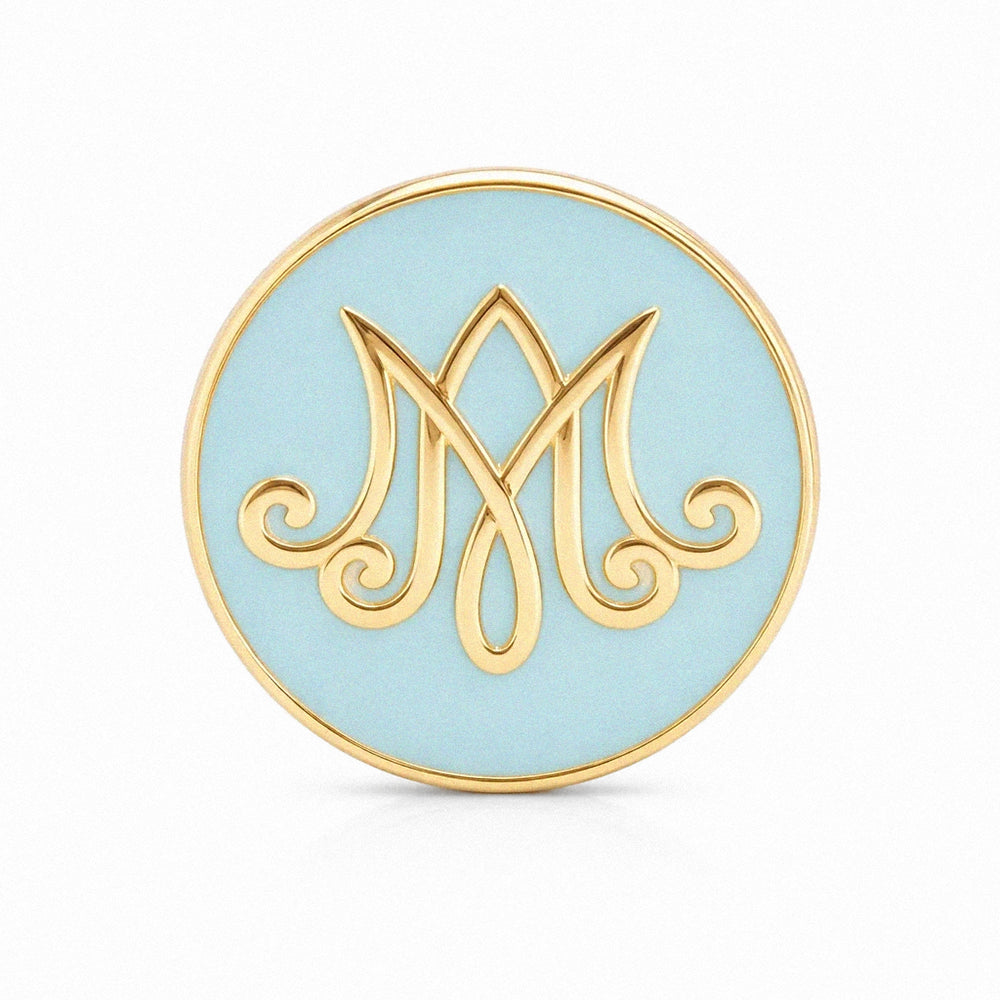 Round blue and gold decorative item with a stylized 'M' design on a white background