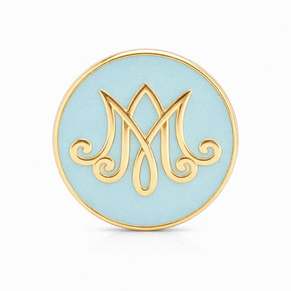 Round blue and gold decorative item with a stylized 'M' design on a white background