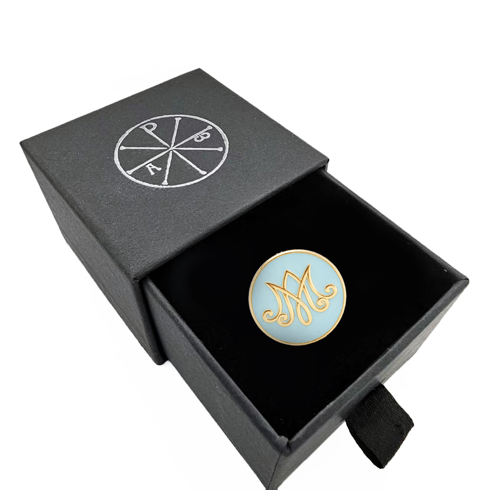 Round decorative item with gold and blue design in a black box with a logo on a white background