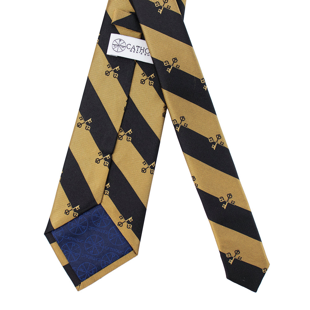 Black and gold striped tie with a blue patch, branded 'Catholic', on a white background. Catholic Men's Shop classic tie.