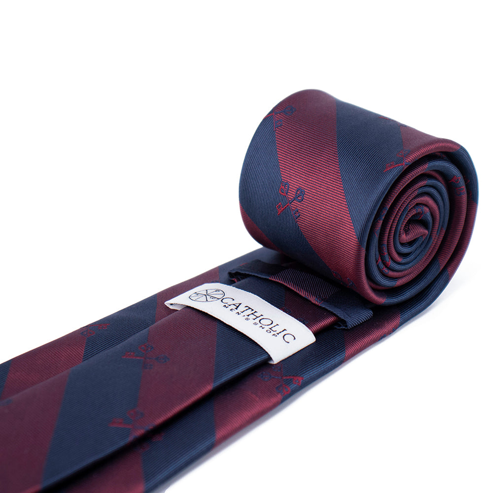 Rolled-up red and blue patterned tie with a brand label on a white background. Premium Catholic gift.